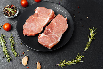 Fresh pork chops on black plate with herbs and spices on dark background