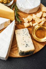 Delicious assorted cheeses with honey and olives on a wooden board display
