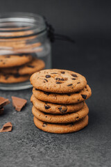 Delicious chocolate chip cookies stacked on a dark surface with chocolate pieces