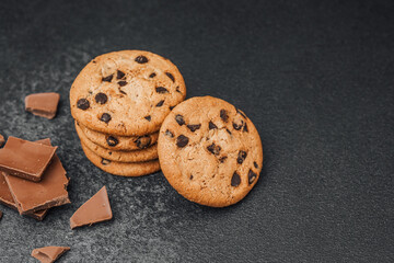 Freshly baked chocolate chip cookies on a dark surface with chocolate pieces