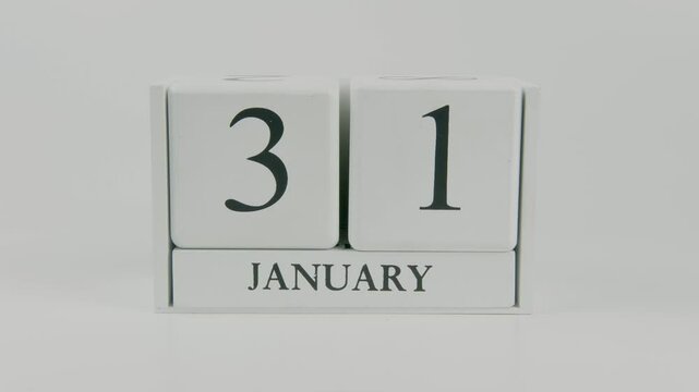 A hand flips a wooden calendar from January 31st to February 1st on a white background, marking the passing of time and the start of a new day