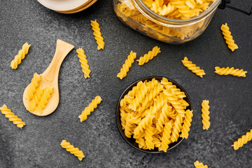Twisted pasta spirals arranged on a dark kitchen countertop with wooden utensils