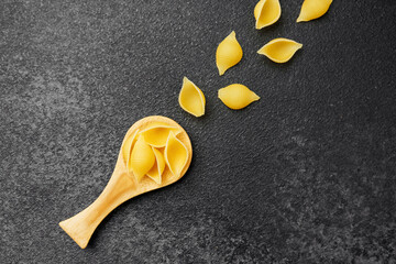 Pasta shells arranged with a wooden scoop on a dark textured background