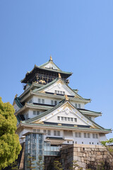 Naklejka premium Osaka, Japan - April 14, 2024: Osaka Castle, a famous Japanese landmark, surrounded by pink sakura trees under a blue sky.