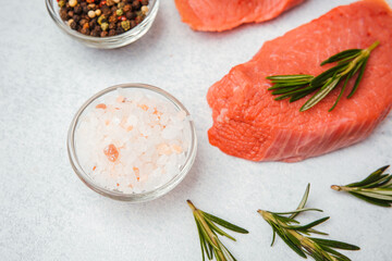 Close-up of pink Himalayan salt, pepper, and raw veal steak with rosemary on white background