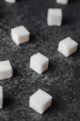 Cubes of white sugar scattered on a dark stone surface with texture