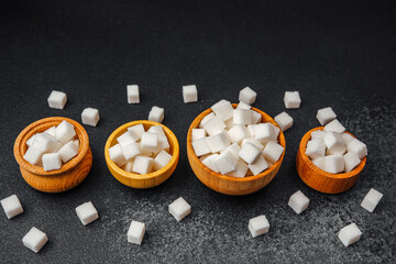 Sugar cubes arranged in wooden bowls on a dark surface show diverse quantities