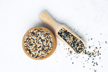 Various seeds arranged in a wooden bowl and scoop on a light background