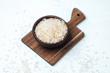Rice in a wooden bowl on a cutting board with scattered grains