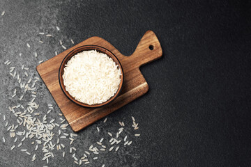 Bowl of uncooked white rice on wooden cutting board with scattered grains
