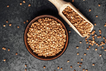 Buckwheat grains in a bowl with a scoop on a dark textured surface