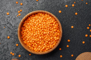 Red lentils in a wooden bowl on a dark surface with scattered lentils