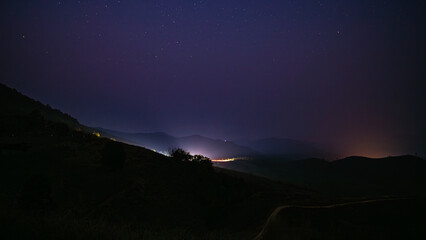 Landscape at night with lights from cars and mountains and stars in the sky.