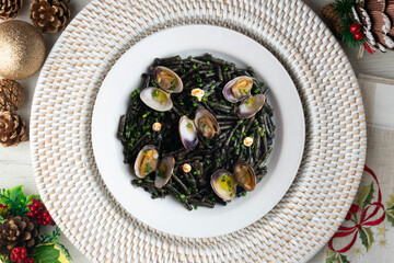 Spanish black fideua. Traditional tapas recipe of noodles with clams and garlic oil. Top view table with christmas decorations.