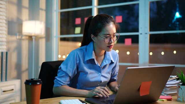 An ambitious Asian businesswoman works late at her desk, focused on sales, planning, and analysis under tight deadlines in a modern office.
