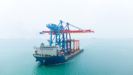Aerial view of a heavy lift vessel transporting massive port cranes across turquoise waters....