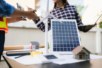 Architects and engineers collaborate at a desk with blueprints and solar panels, planning...