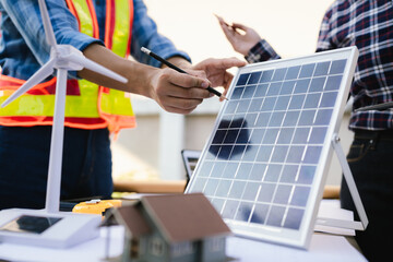 Architects and engineers collaborate at a desk with blueprints and solar panels, planning...