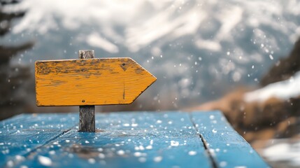 A wooden arrow sign pointing to the right on an old blue wooden table with blurry snow-capped mountains in the background