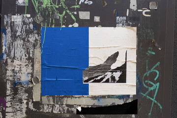 Urban street collage with torn posters, blue and white ripped paper textures on grungy black wall.
