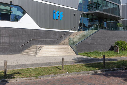 Modern office building with the blue IFF logo (International Flavors Fragrances) prominently displayed near the entrance with stairs and greenery. Oegstgeest, Netherlands, 3 May 2025