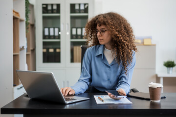 Confident Russian businesswoman sits indoors at her desk, dressed in formal attire,  paperwork and planning. Stylish and efficient, she manages tasks, notes ideas, and leads with professionalism.