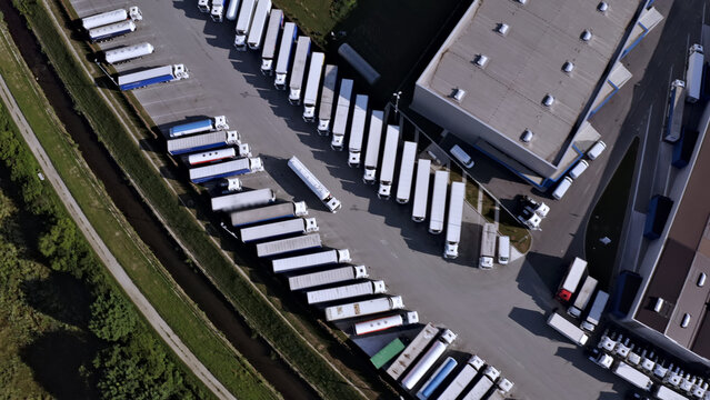 Aerial view of a bustling freight yard, showcasing rows of parked trucks and cargo containers, symbolizing efficient transportation and logistics operations.