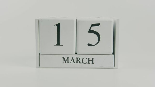 A hand flips a wooden calendar from October 15th to October 16th on a white background, marking the passing of time and the start of a new day