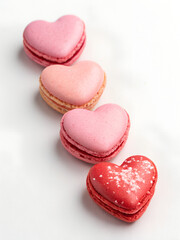 Fototapeta premium Four heart-shaped macarons in pink and red are arranged diagonally on a white surface