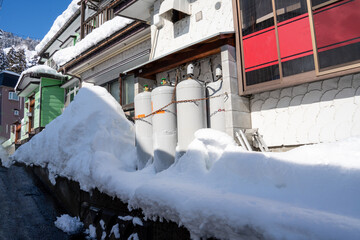 Snow-covered LPG gas cylinders lined against the side of a traditional Japanese house during...