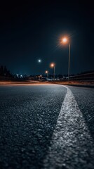 Low angle view of empty asphalt road illuminated by street lights at night in urban area under dark sky with moon