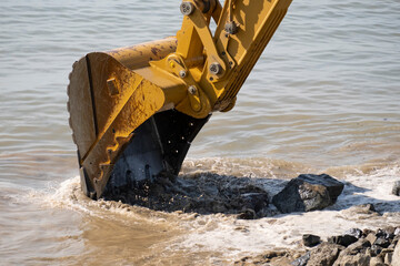 Excavator removing debris from water at construction site near riverbank during bright daylight