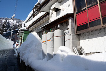 Snow-covered LPG gas cylinders lined against the side of a traditional Japanese house during...