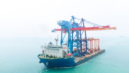 Aerial view of a heavy lift vessel transporting massive port cranes across turquoise waters....