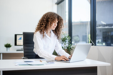 Confident Russian consultant sits at modern desk, analyzing market data on laptop. reports and...