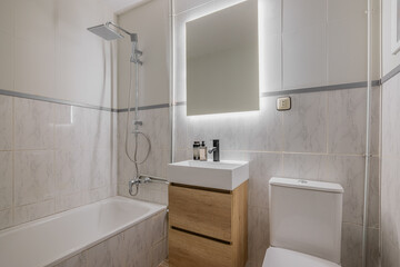 Bathroom with marble tile walls wood vanity white sink backlit mirror and overhead rain shower fixture