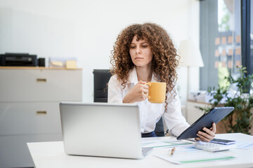 Fototapeta premium Confident Russian consultant sits at modern desk, analyzing market data on laptop. reports and charts, she embodies precision, leadership, and strategic mindset of corporate consulting.