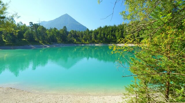 Alpine beach at Urisee Lake in Tirol with turquoise water, green forest hills, and mountain views, relaxing holiday destination