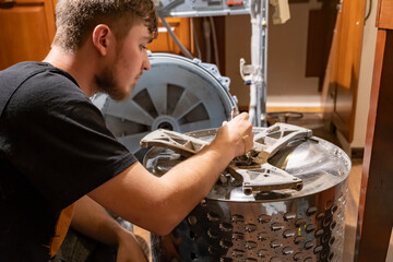 Young man repairing a washing machine in a home kitchen during the afternoon