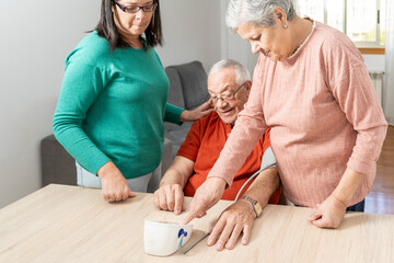 Elderly man taking blood pressure with tensiometer, supported by his wife and daughter in a cozy home environment
