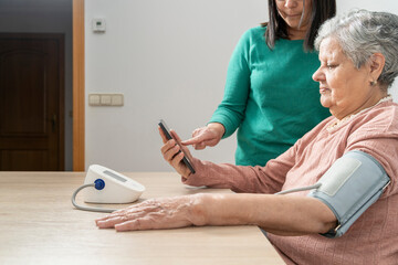 Nurse helping an elderly woman taking blood pressure with a tensiometer and checking results on a smartphone