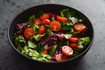Salad with green and purple leaves and cherry tomatoes in black bowl