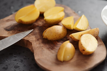 Raw washed and chopped baby potatoes ready to cook on olive wood board
