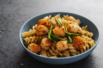 Fusilli pasta with scallops and asparagus in blue bowl on concrete surface