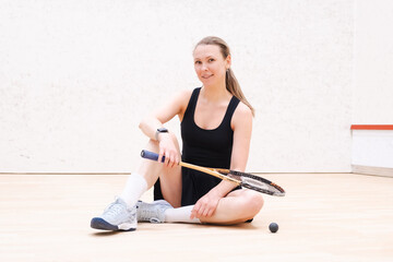 Confident female squash player sits on a court holding a racket, showcasing athleticism and...