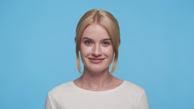 Confident young woman winking playfully at camera on blue