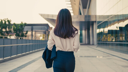 Rear view of Asian finance advisor walking confidently in business district, holding blazer. Modern...