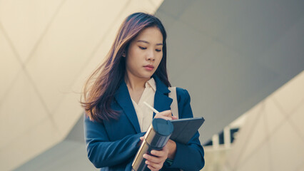 Asian businesswoman focused on using a digital tablet with stylus in an urban setting. Professional...