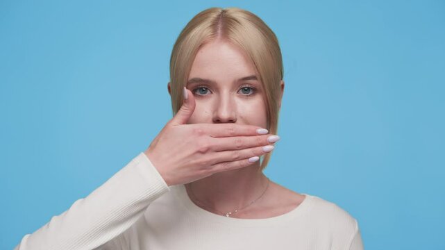 Woman covering mouth with hand in silence gesture on blue