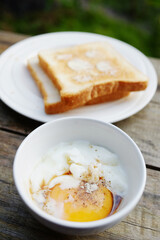 Soft boiled eggs in white bowl and buttered toast in white dish for breakfast on wooden table